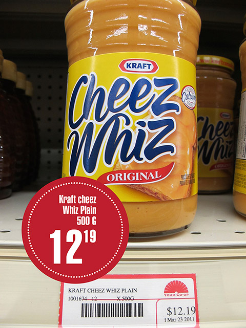Un pot de produit de formage fondu de marque Kraft Cheez Whiz de 500 grammes repose sur un étalage. Une étiquette précise son prix de vente de 12,19 $.