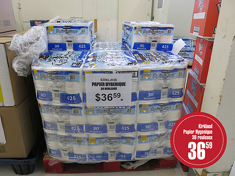 Kirkland brand toilet paper packages, wrapped in plastic, rest on a transport pallet. A poster specifies the price of $36.59 for 30 rolls, each containing 425 sheets.